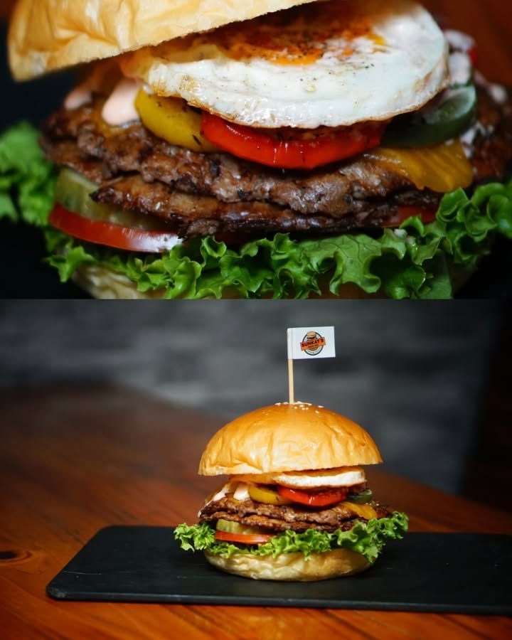 Burger bò hai tầng kẹp trứng ốp la, cà chua, đặt trên khay đá phiến cắm cờ thương hiệu Burger bò hai tầng kẹp trứng ốp la, cà chua, đặt trên khay đá phiến cắm cờ thương hiệu